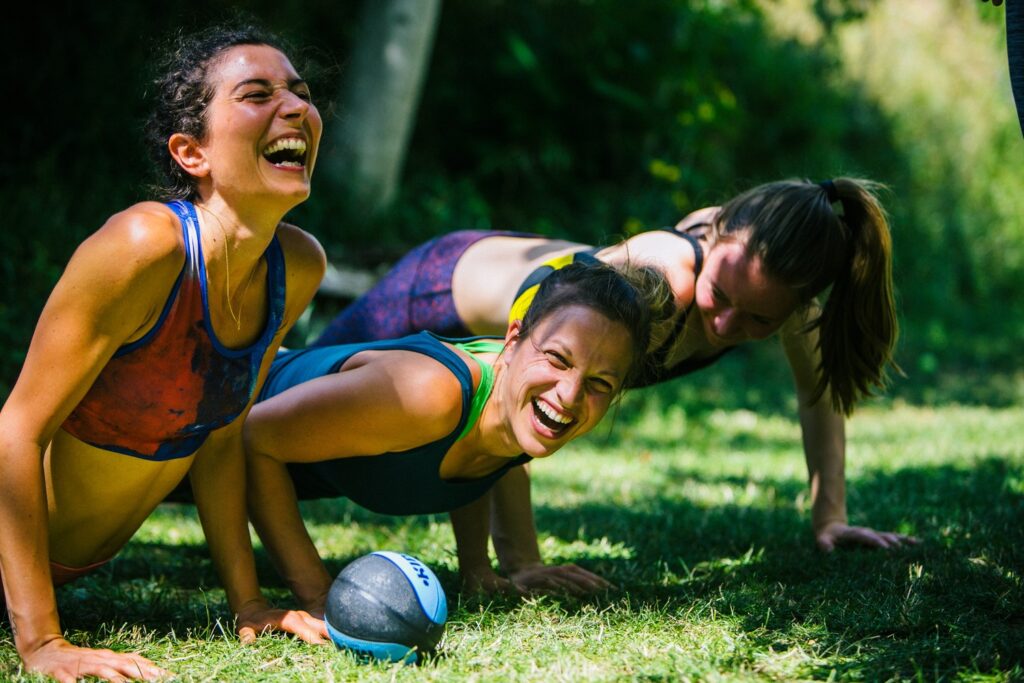 Three girls doing pushups during an AcroYoga warmup game in the grass.