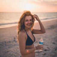 Girl holding a bottle of water at the beach.