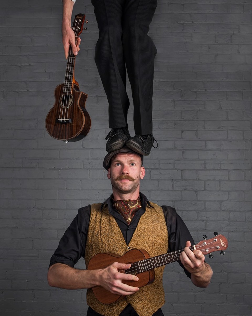 Guy playing ukulele while another person standing on his head