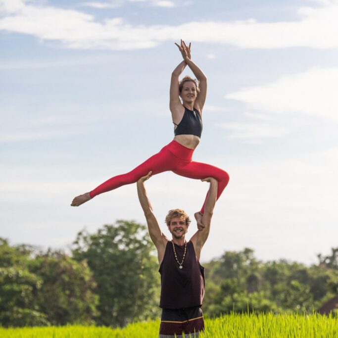 Beautiful AcroYoga pose in a field of grass. Man standing tall, girl posing in a elegant pose.