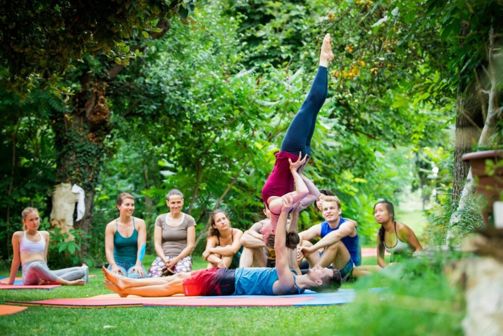 Teachers showing how to balance upside down during an AcroYoga retreat in the garden. Students having fun watching them demo an AcroYoga position.