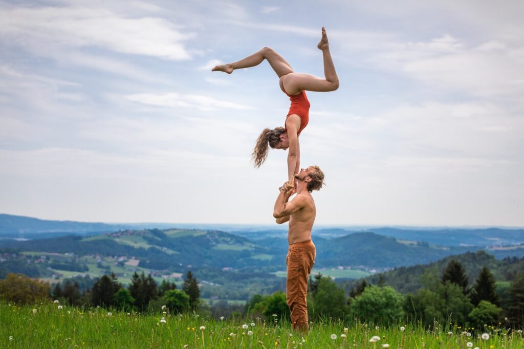 Two people practicing standing AcroYoga. Girl ontop making a beautiful shape with her legs. The background beautiful hills in Austria.