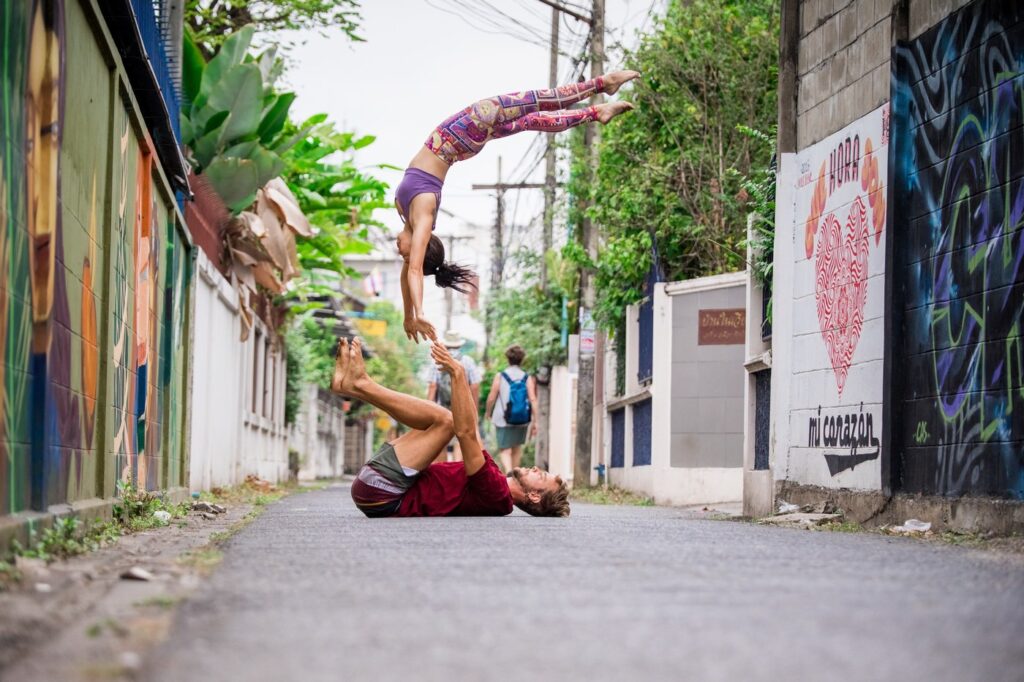 Girl flying high in an AcroYoga pop on the street. Graffitiy and bushes in the background.