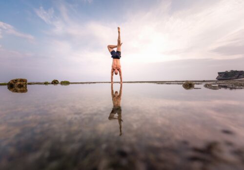 man doing a handstand on the beach with water reflection