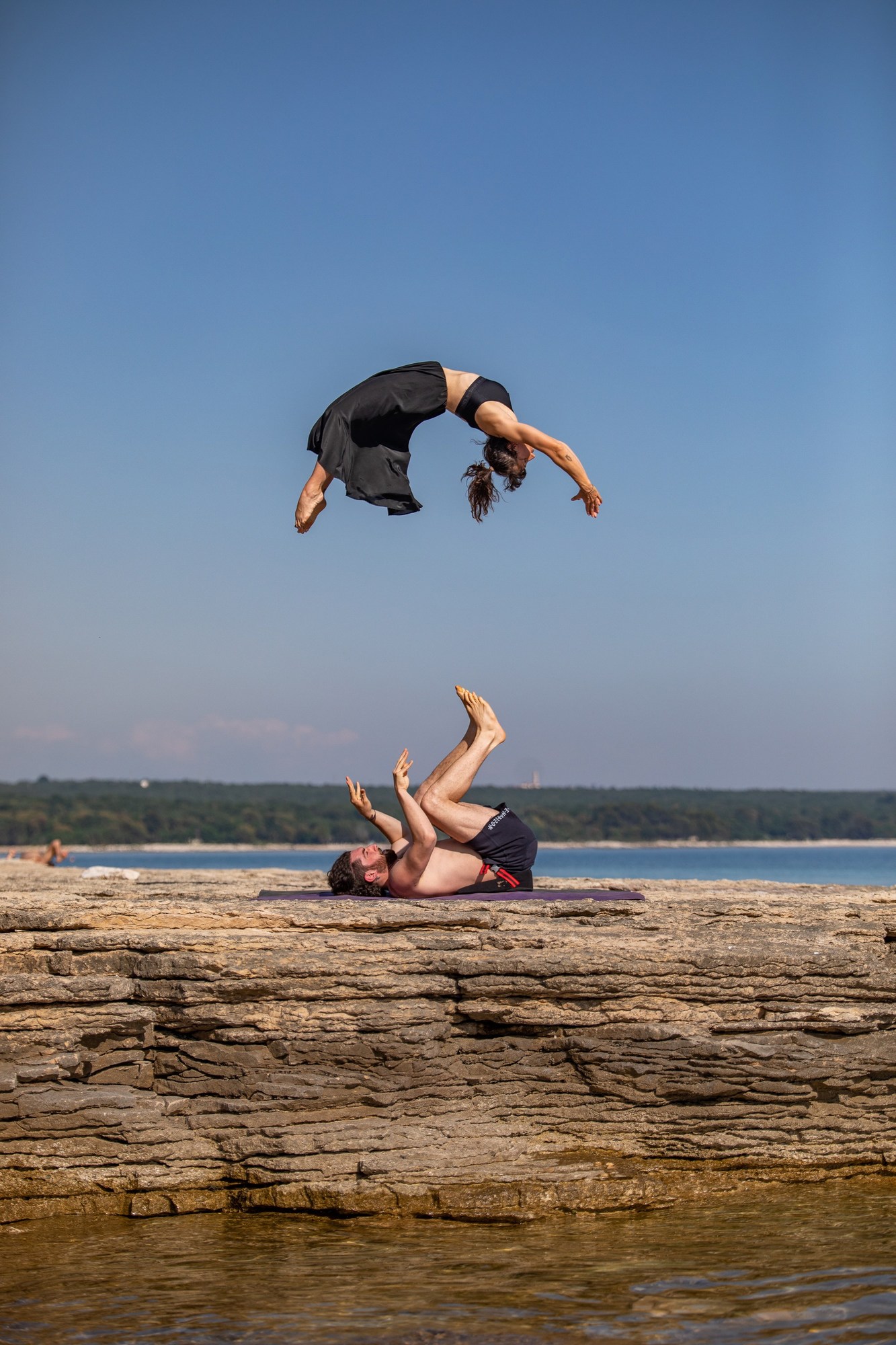 Couple doing a crazy flip along the Croatian coast. Girl is wearing a black dress that flies in the wind.