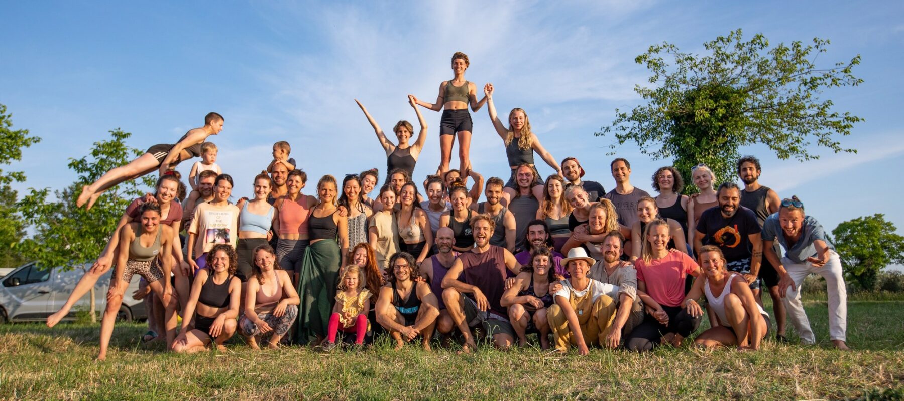 A big group of people standing next to each other smiling into the camera, celebrating life during our AcroYoga gathering.