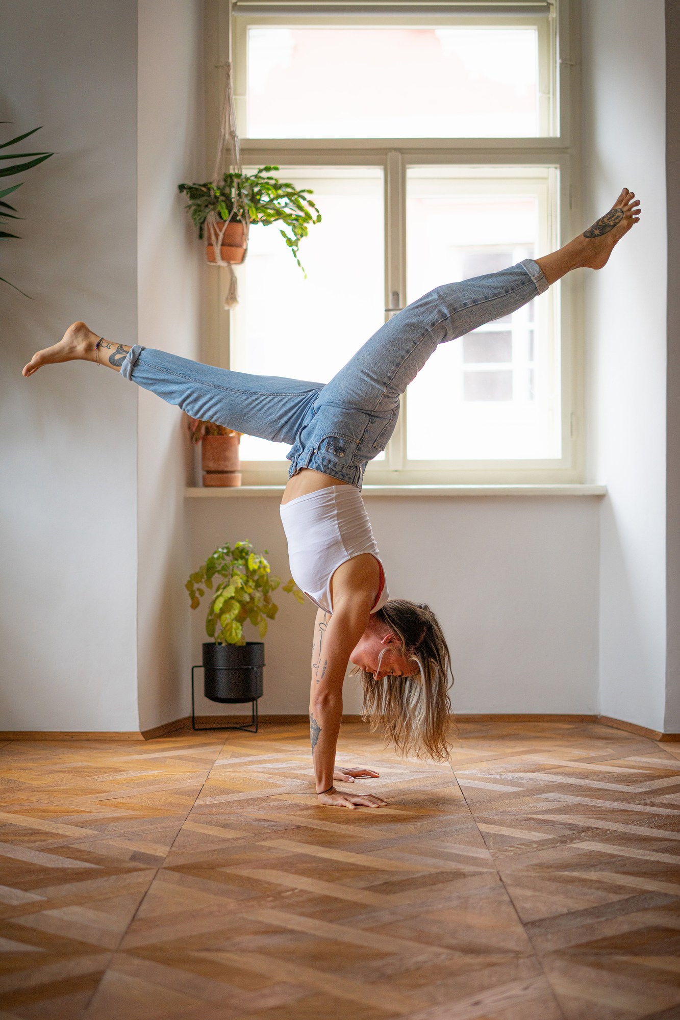 Girl doing a handstand in a room with wooden floor wearing jeans.
