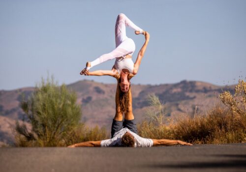 AcroYoga pose on the road with plants and mountains in the background.