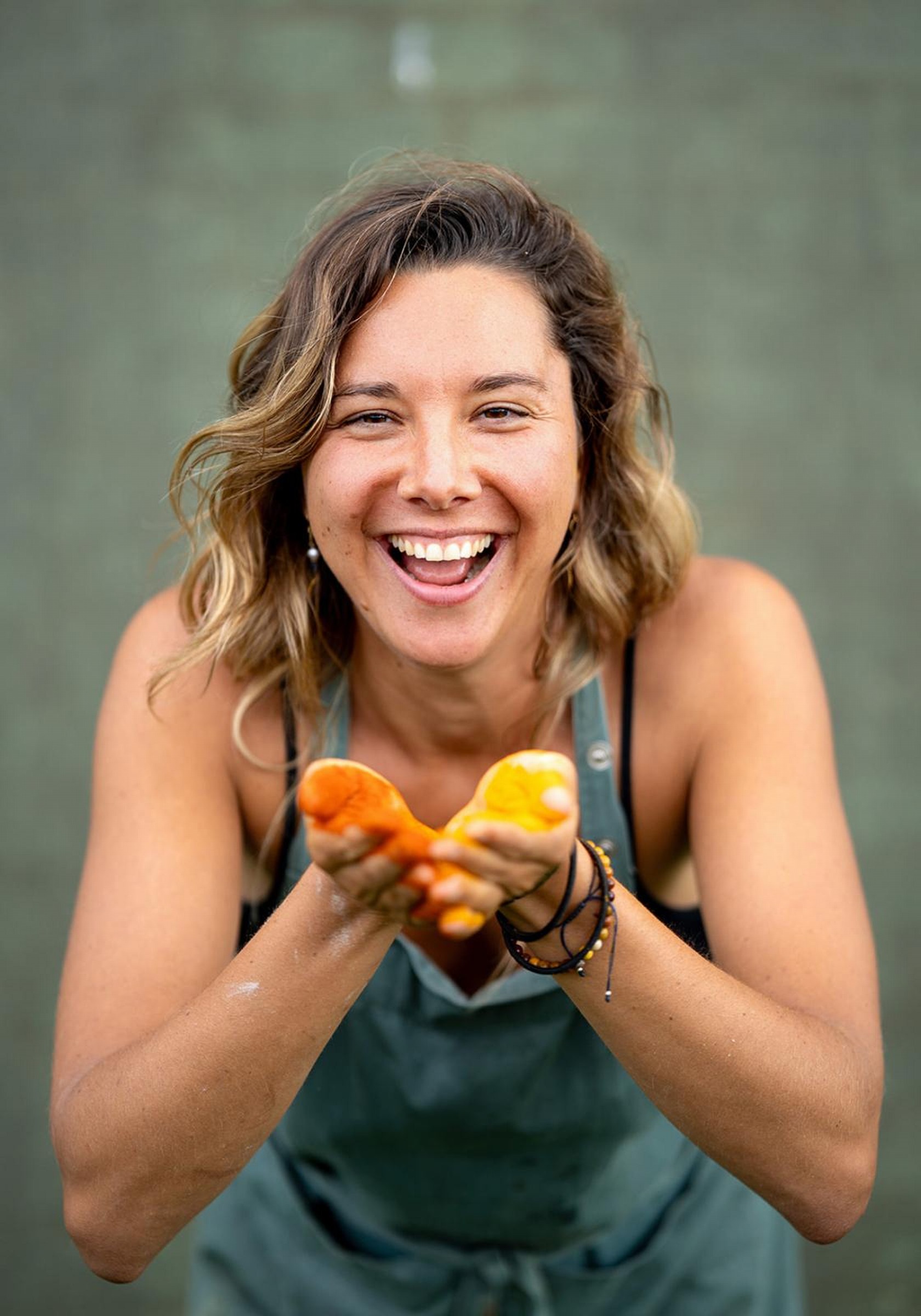 Girl smiling into the camera while holding yellow powder in her hands during a cooking session.